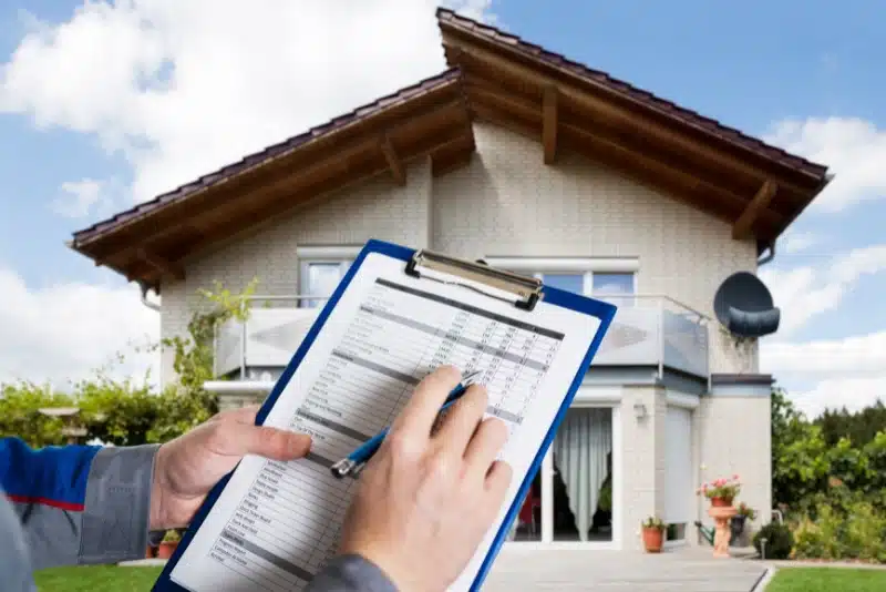 What Are the SB 721 California Law Requirements—& Why Are Investors Nervous Inspector holding a clipboard with a checklist in front of a two-story suburban home with a satellite dish and wooden roof beams.